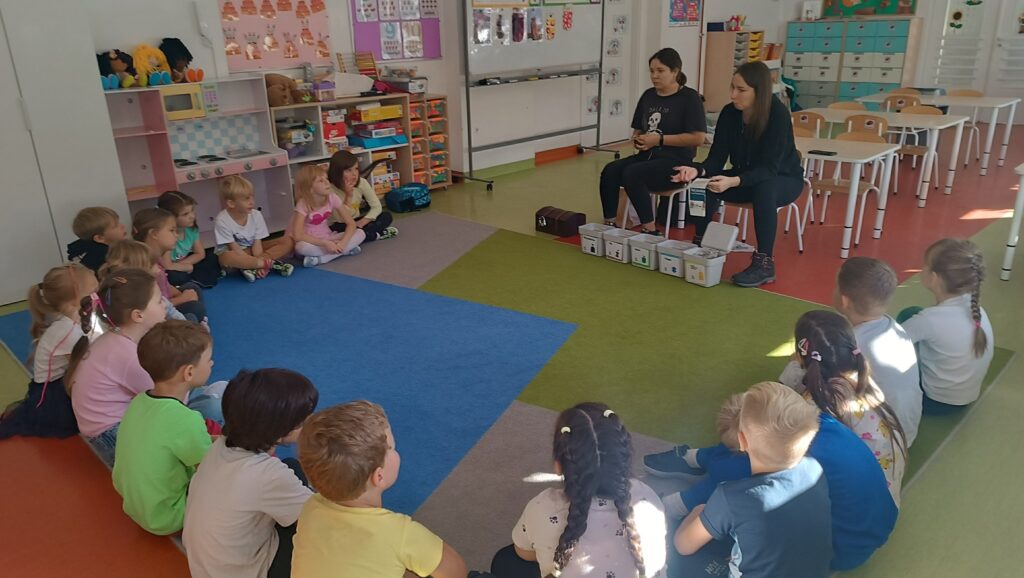 Prowadząca tłumaczy dzieciom zasady segregacji odpadów podczas zajęć edukacyjnych