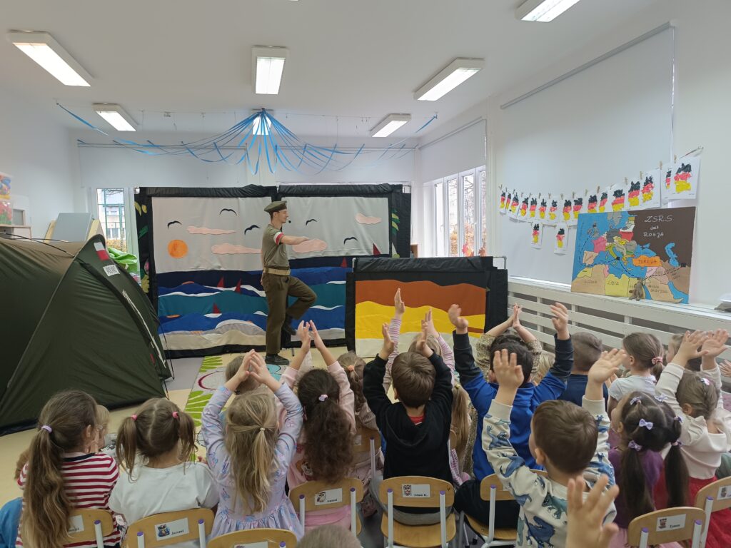 dzieci siedzące na krzesełkach, żołnierz maszerujący