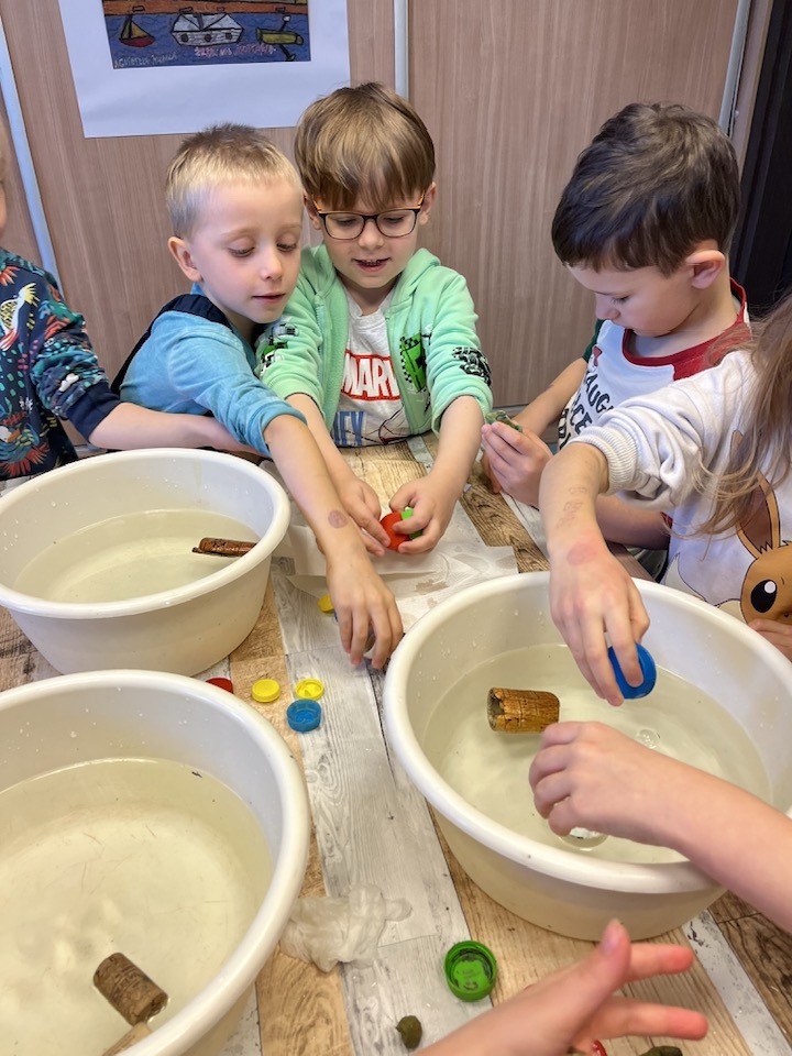 grupa dzieci sprawdza w miskach z wodą co pływa a co tonie